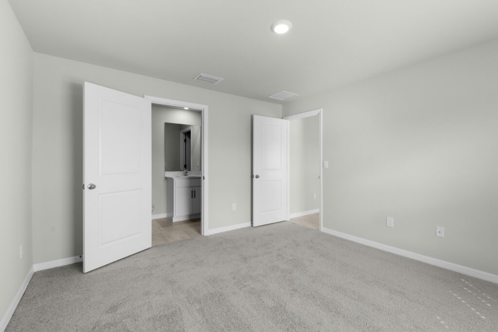 Contemporary empty bedroom interior with beige carpet and open doors leading to bathroom.