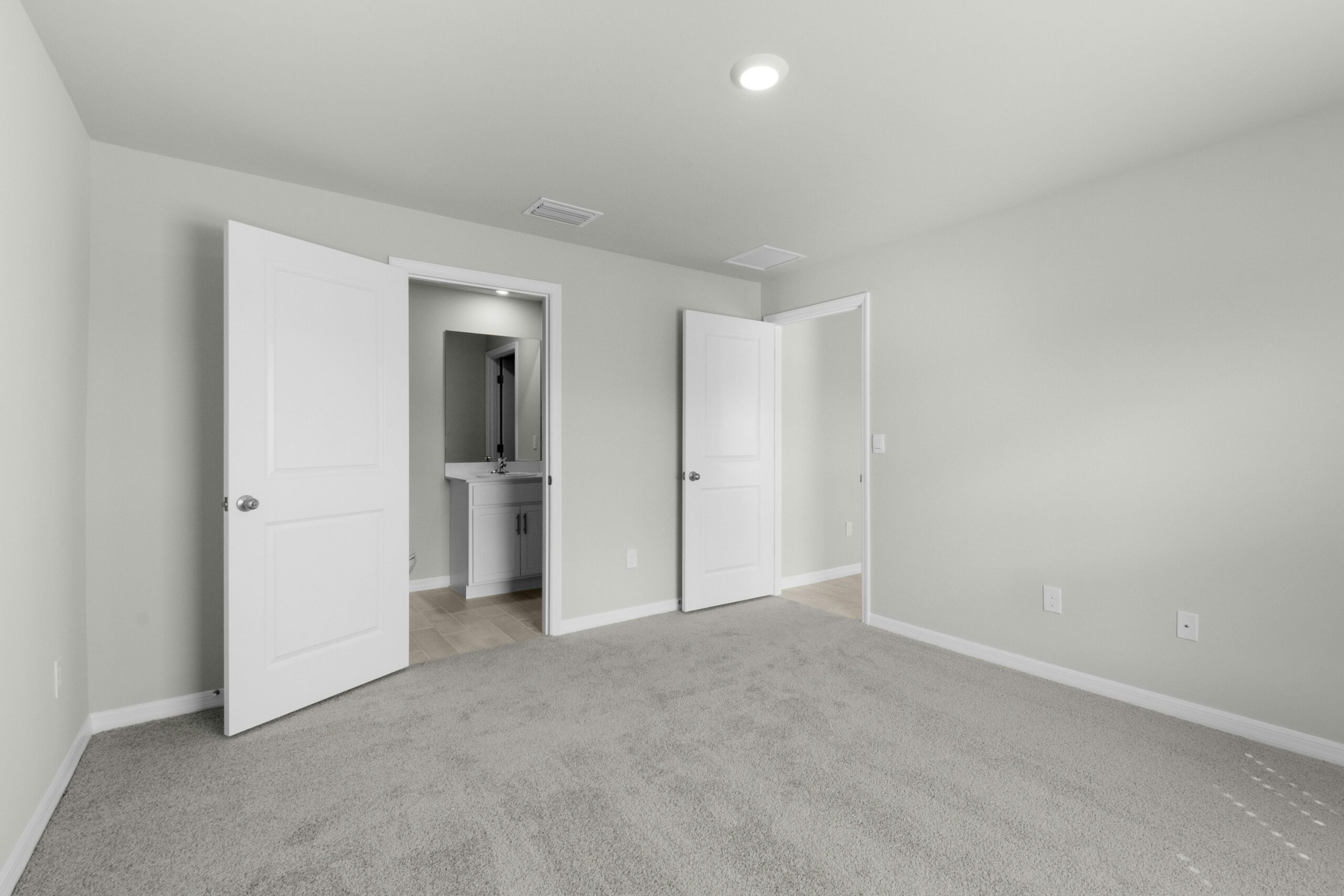 Contemporary empty bedroom interior with beige carpet and open doors leading to bathroom.