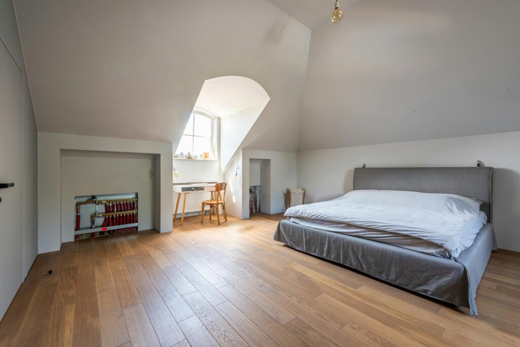 Spacious modern attic bedroom with wooden floors and cozy furnishings.