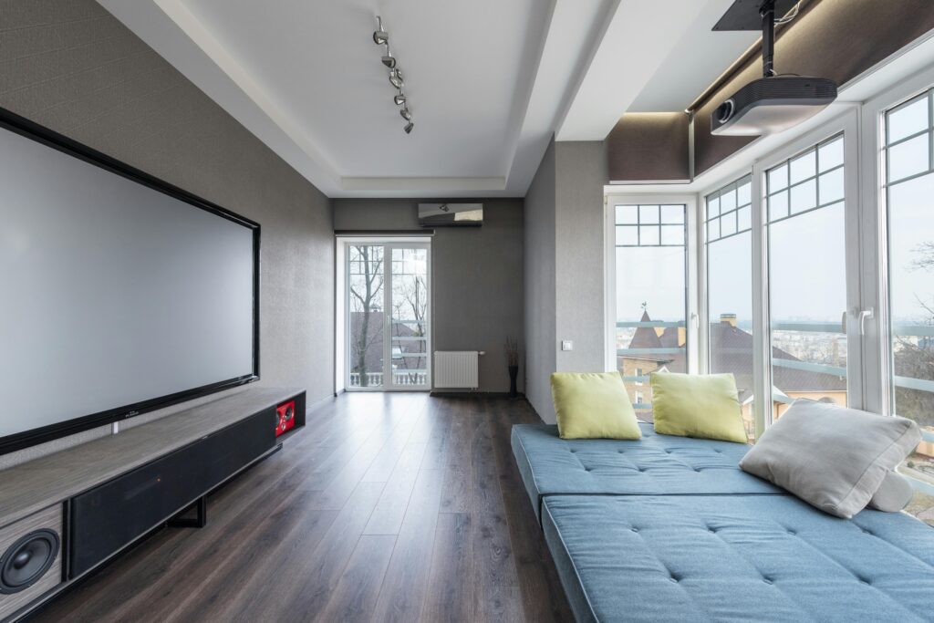 Comfortable settee with colorful cushions placed near big windows against contemporary television set in spacious room of modern stylish apartment