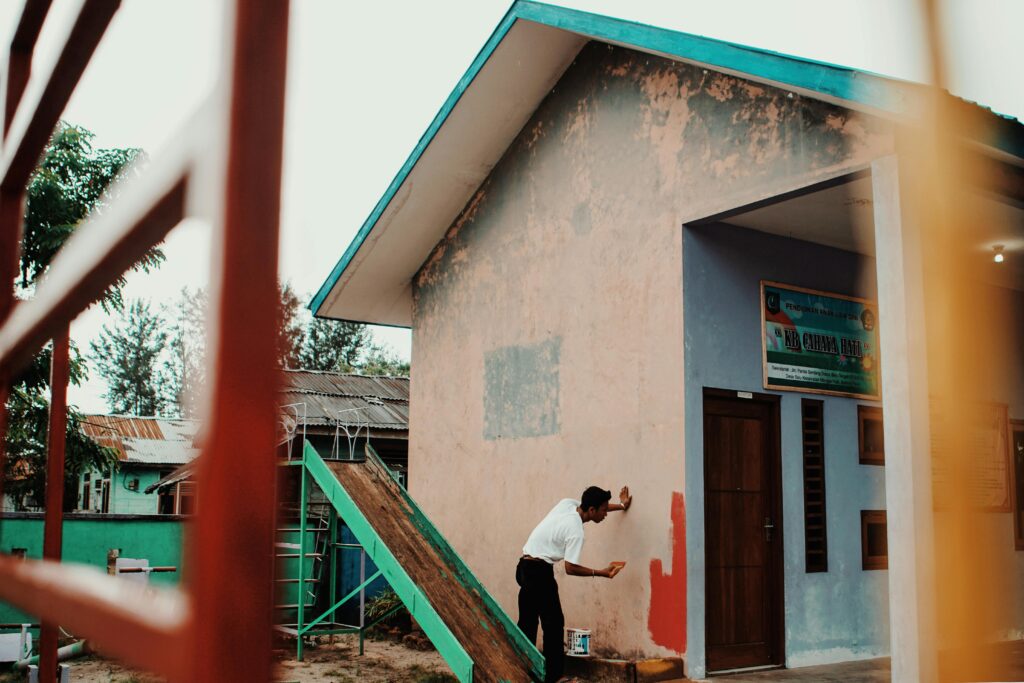 A person painting a building's exterior wall outdoors during the day.